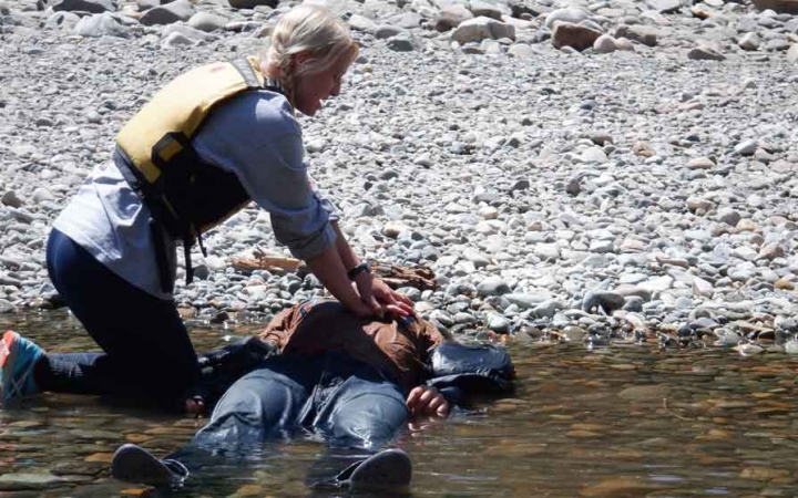 a person lays in shallow water while another practices medical skills on them during a wilderness first aid course with outward bound